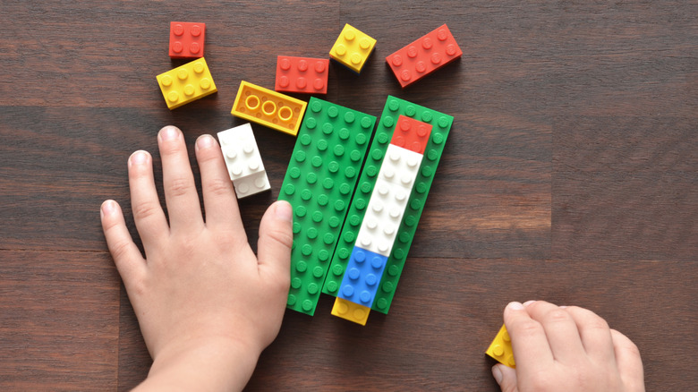 A child's hands playing with multi-colored Legos on a table.