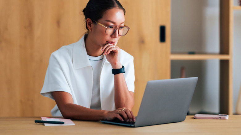 Woman in a white shirt and glasses researching options on a laptop