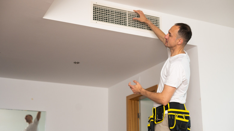 HVAC technician checking a vent located on a wall.