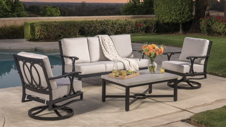 A black metal and cream patio set by a pool during sunset