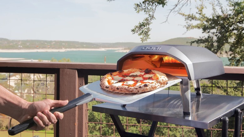 A person removing a pizza form an Ooni Koda pizza oven
