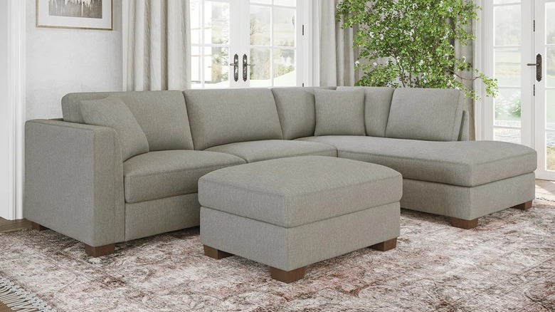 A small beige sectional with storage ottoman in front