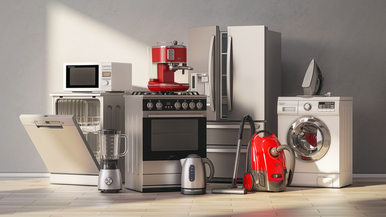 A series of home appliances gathered in a room, including a dishwasher, an oven, a washing machine, a fridge, a vacuum cleaner, and small kitchen appliances