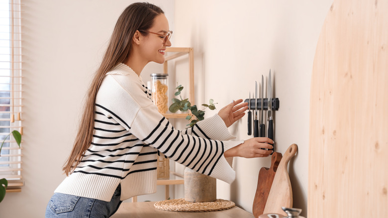 Young woman taking knife from magnetic holder on light wall in kitchen