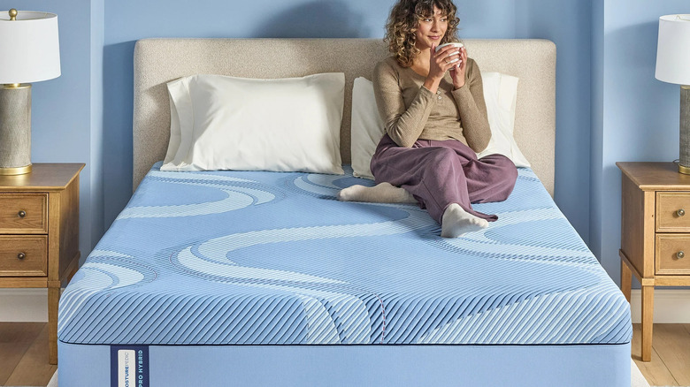 A woman sitting on a Sealy Posturepedic Pro Omak Valley 13" Firm Hybrid Mattress