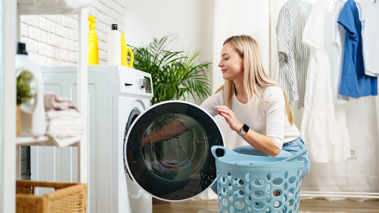 A woman putting clothing into a washer in a laundry room