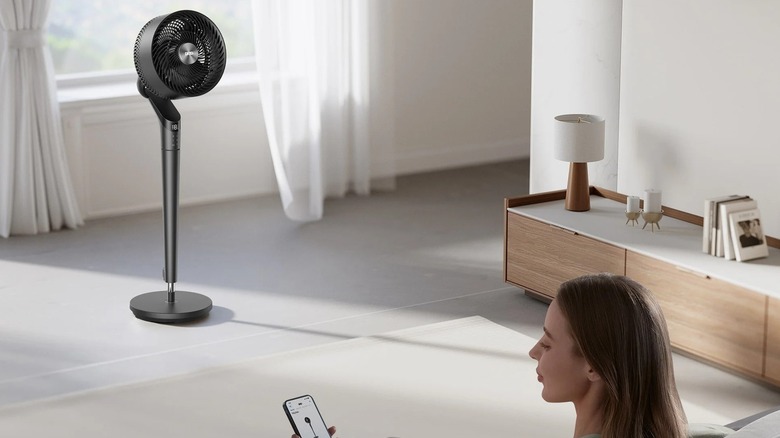 Woman controlling the DREO TurboPoly 350S Pedestal Fan from an app on the phone while sitting in a living room