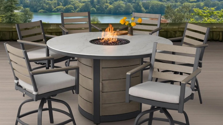 An outdoor dining table with a fire feature with chairs on a patio.