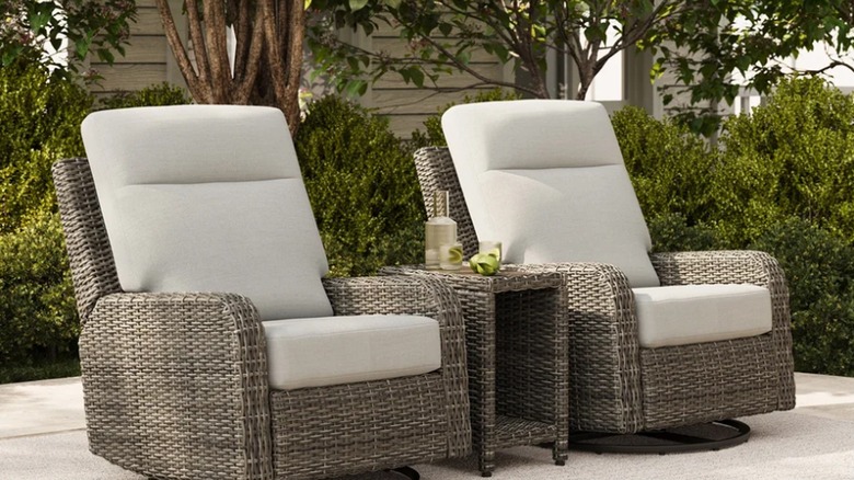 Two faux-wicker outdoor recliners and a table with drinks sit on a patio.