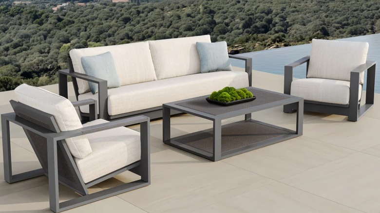 A cream-colored outdoor couch, chairs, and coffee table sit on a patio with a view.