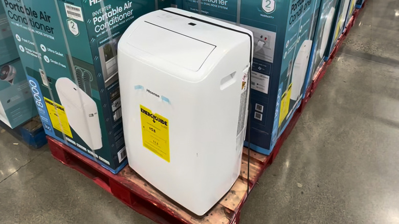 A portable air conditioning unit on a pallet in a Costco warehouse store, surrounded by boxes