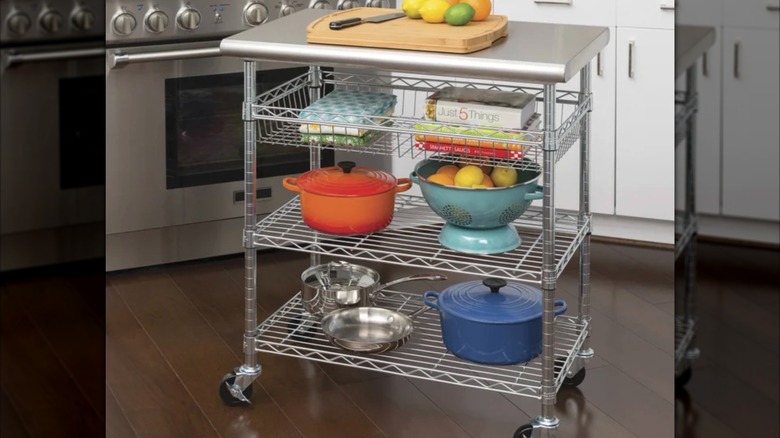 Product image of Seville Classics Stainless Steel Kitchen Cart with cutting board on the counter top, books and kitchen appliances on each shelf