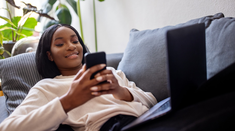 Woman laying on a sofa smiling at her phone