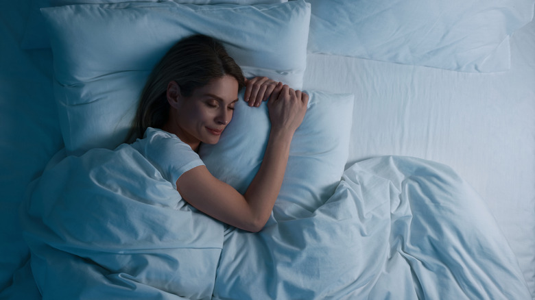 Woman sleeps comfortably underneath a white comforter