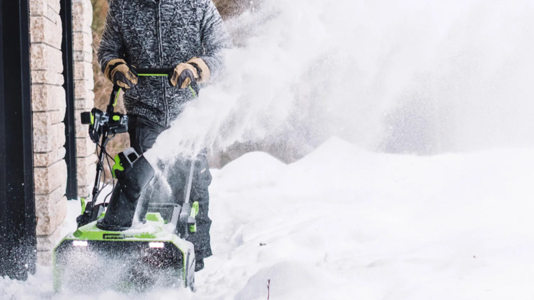 Man pushing Greenworks snow thrower along garage