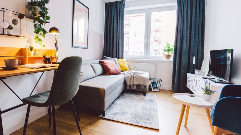 Small living room with low sofa chaise on small rug next to narrow desk and chair