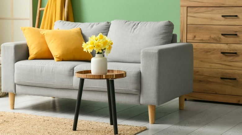 Gray modern two-seater sofa with yellow pillows sitting in front of wood chest of drawers