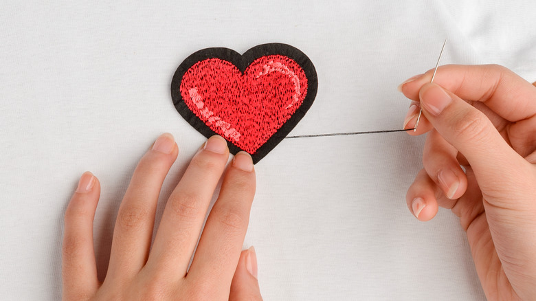 Hands sewing heart-shaped patch