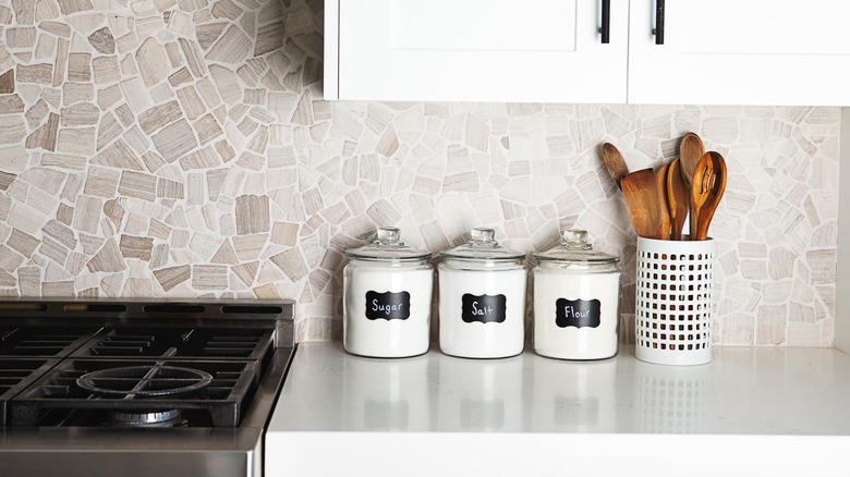 A few clear canisters on the counter next to a utensil holder
