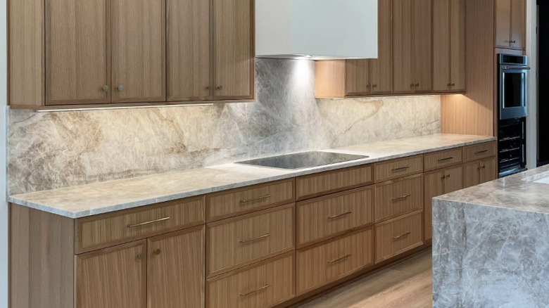 A multicolored quartz countertop and matching backsplash with a built in stovetop and white oak cabinets.