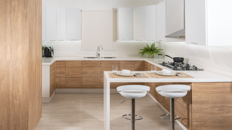 A minimalist kitchen with white oak cabinets, white countertops and white bar stools at a breakfast nook.