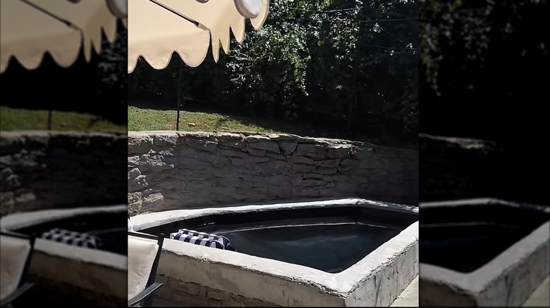 A triangular-shaped pool that rests up against a stone wall.