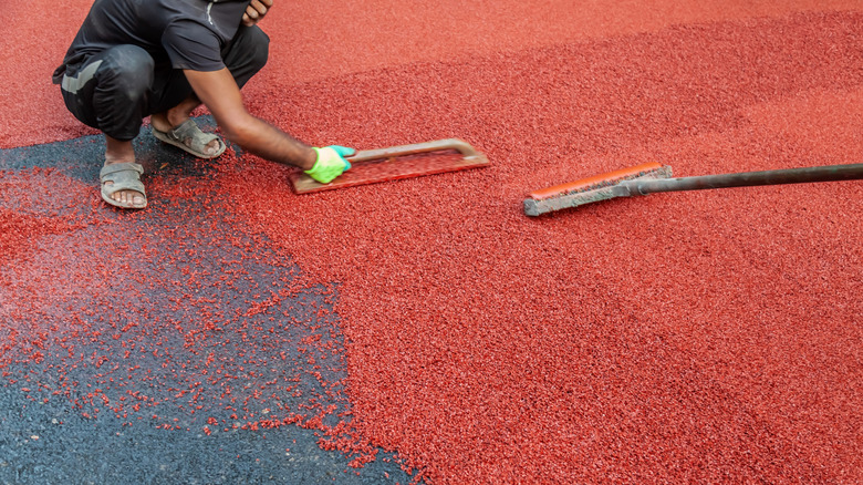Man smooths over red rubber surfacing on pavement