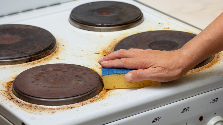 Closeup of person's hand with a sponge cleaning a very stained and dirty stovetop