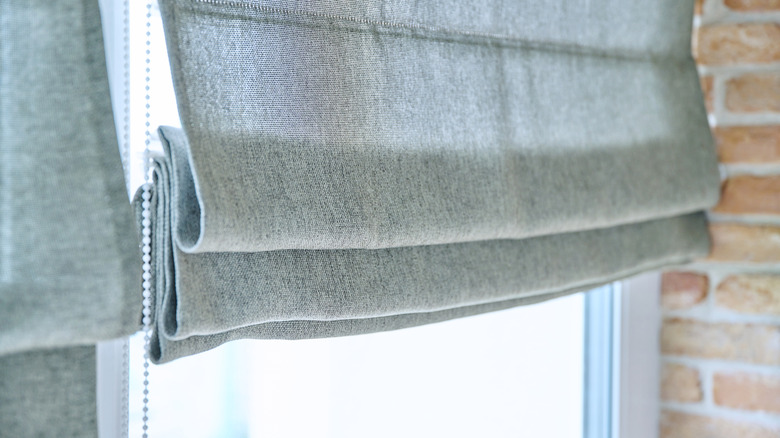 A pleated gray roman shade on a window with a brick wall in the background.