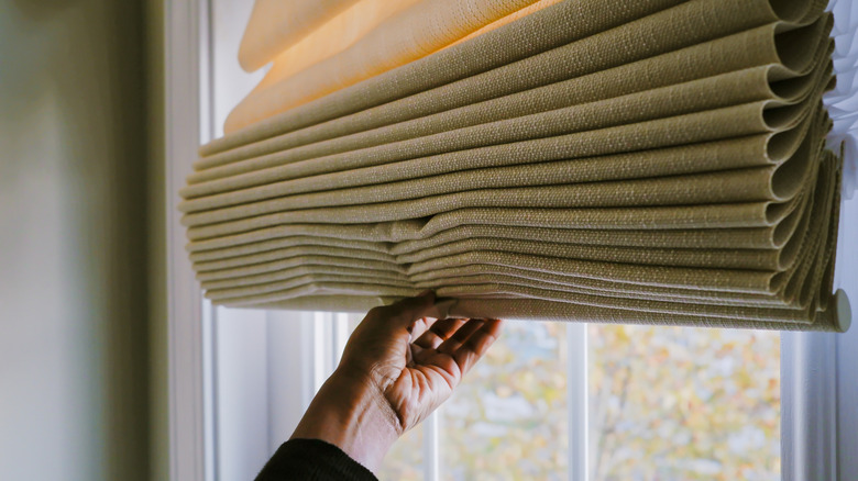 Someone pulling closed some Roman shades.