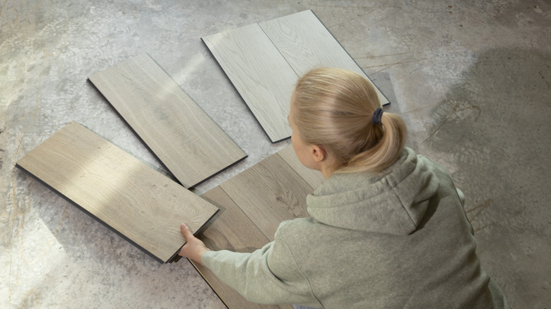 A person holding up different wood tiles on a concrete floor