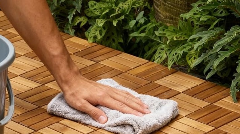 A person using a bucket and rag to wipe down the Thyoi wooden tiles with plants in the background
