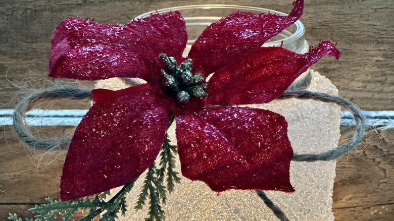 A frosted glass jar decorated with a faux poinsettia and twine.