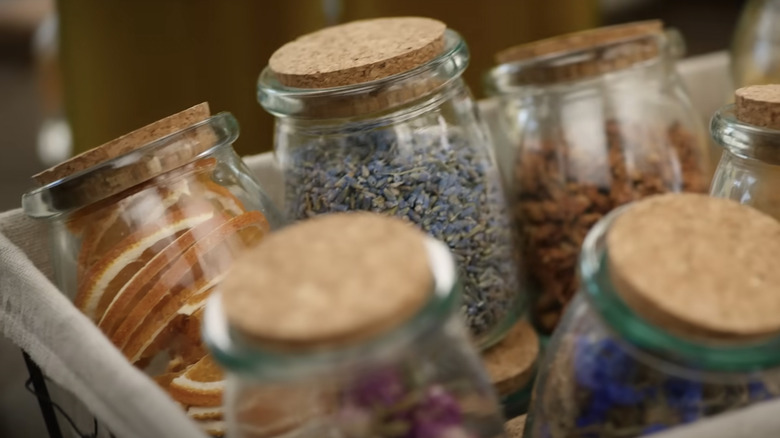 Assorted glass jars with cork lids are filled with dried flower buds and fruits