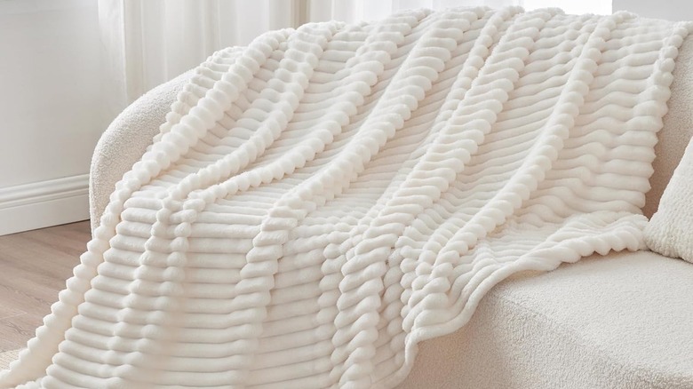 A soft white throw blanket is draped on a boucle upholstered sofa