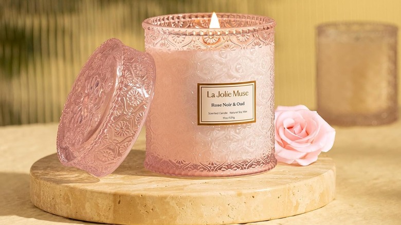 A pink La Jolie Muse Rose Noir & Oud Candle sits on a beige stone countertop