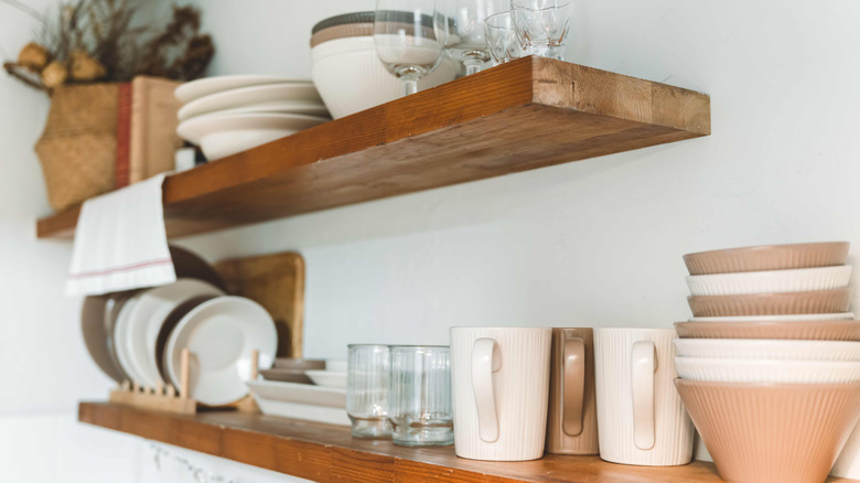 Two wooden floating shelves with an assortment of bowls, plated, glassware, and mugs