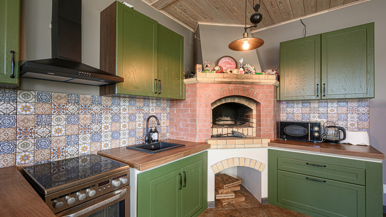 Olive green cabinets and patterned backsplash in a cozy kitchen with a fire oven in the corner
