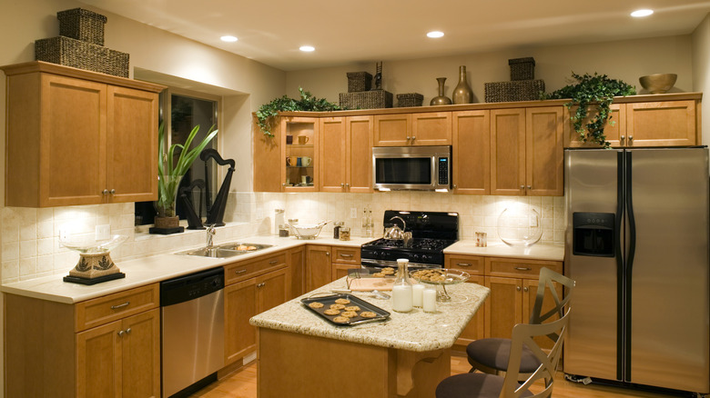 Wicker baskets, trailing plants, and metal bowls and bottles adorning the space above wooden kitchen cabinets in a light kitchen