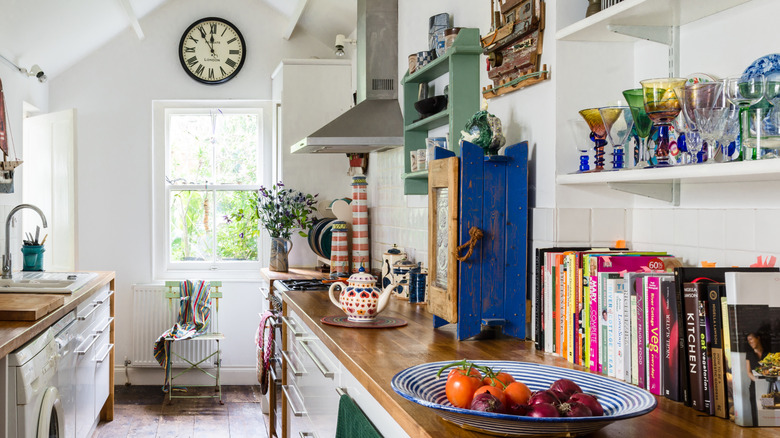 A galley-style kitchen with wooden counters, glassware-filled open shelving, and cookbooks lined up against the white backsplash
