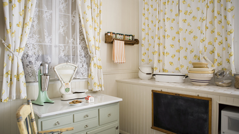 White curtains with a lemon print in a light, cozy kitchen filled with ceramic bowls on the counter