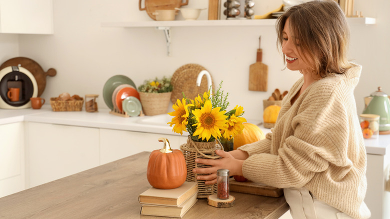 Young woman arranging sunflowers and books in a light kitchen