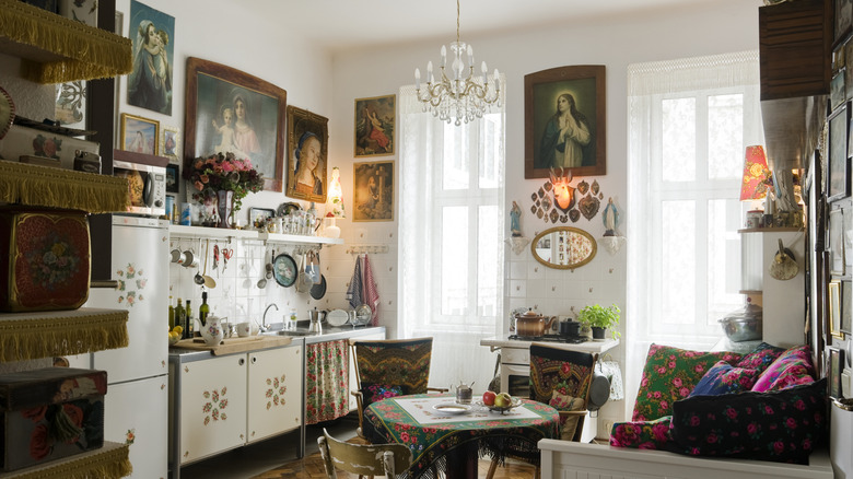White kitchen with framed paintings and mirrors filling the walls and with trinkets on open shelving