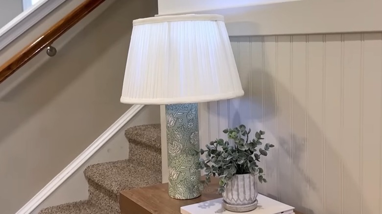 A lamp with floral base on a entryway table
