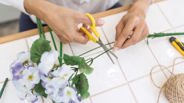 Person cutting a fake flower stem on a table.