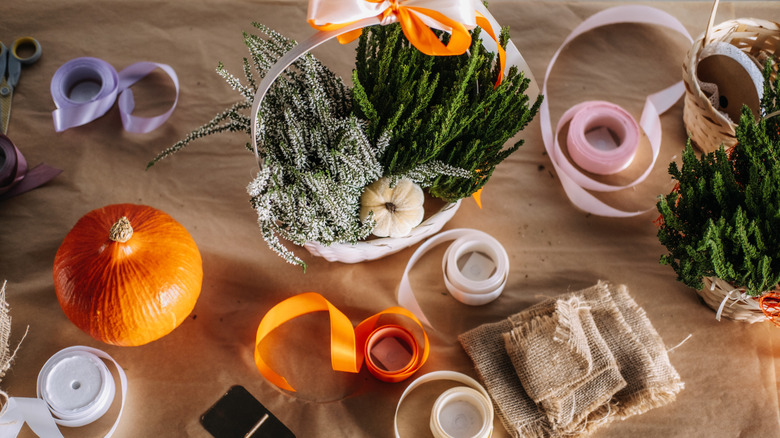 craft table full of fall themed ribbons, a pumpkin, and evergreen foliage