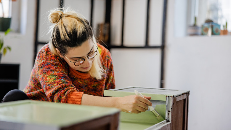 Smiling young woman painting an old cabinet