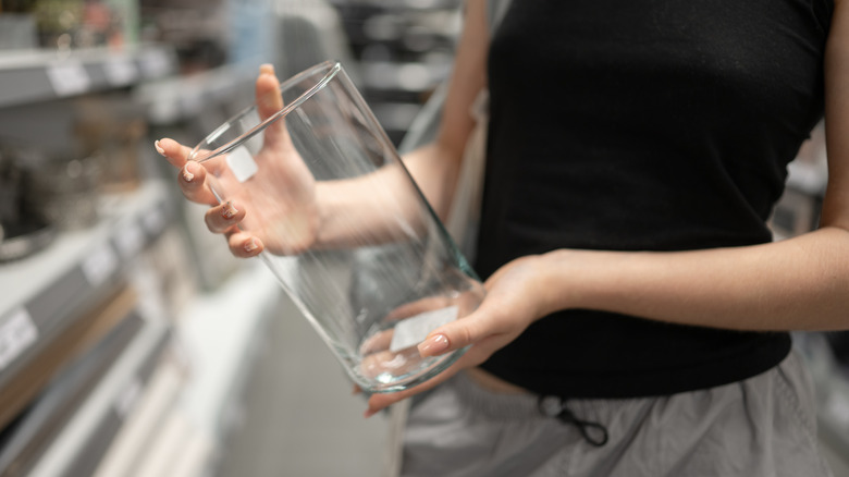 A pair of female hands hold a glass vase at a store.