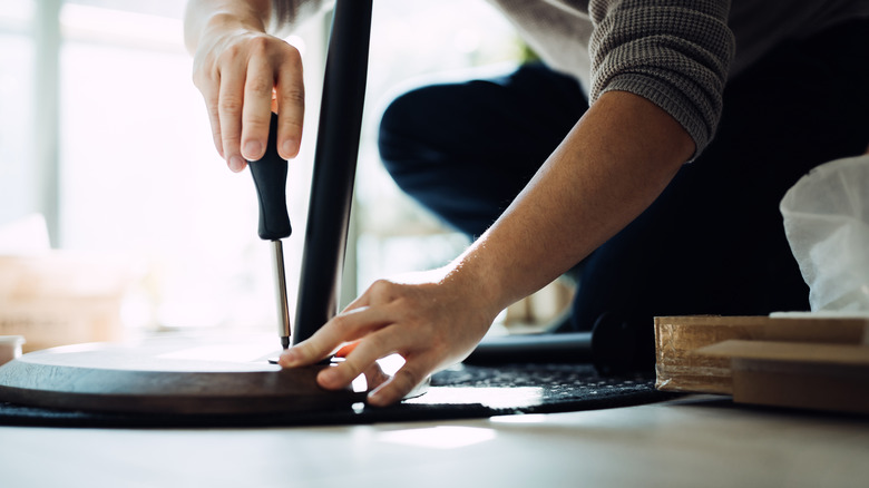 Close up of a man attaching legs to a piece of furniture.