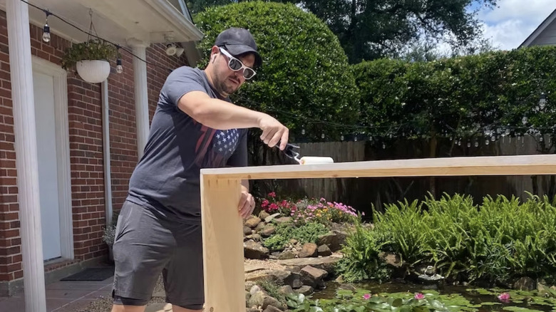 Man outside painting wooden shelf with roller